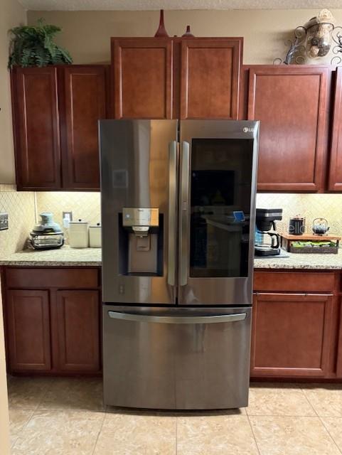 kitchen with light stone countertops, decorative backsplash, stainless steel fridge, and light tile patterned flooring