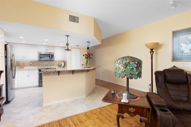 kitchen featuring a breakfast bar area, white cabinetry, backsplash, stainless steel appliances, and light stone countertops