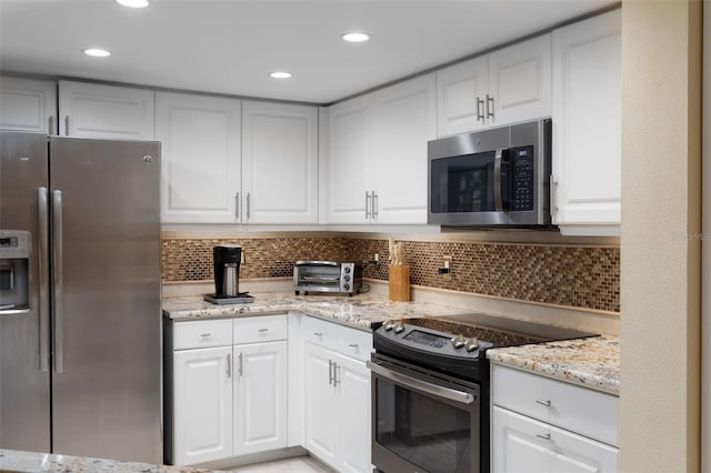 kitchen with decorative backsplash, light stone countertops, white cabinets, and appliances with stainless steel finishes