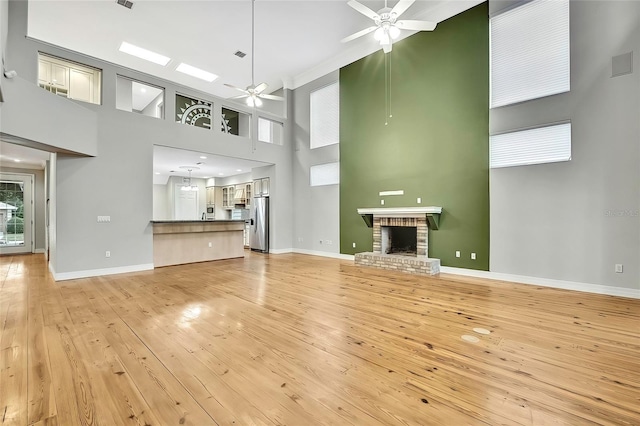 unfurnished living room featuring ceiling fan, a high ceiling, a brick fireplace, and light wood-type flooring