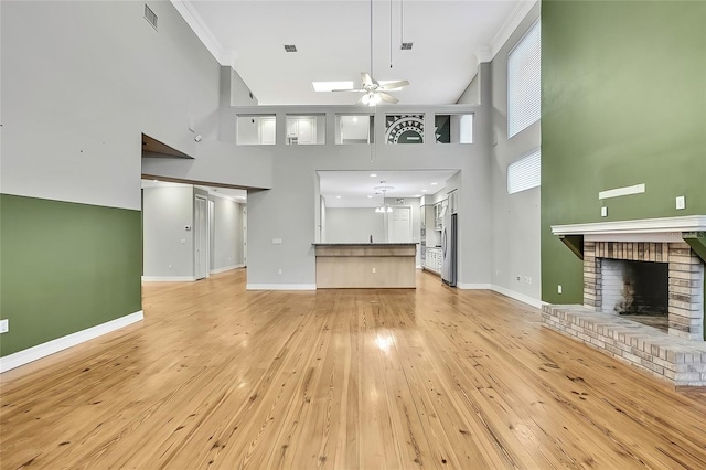 unfurnished living room with light wood-type flooring, a brick fireplace, a towering ceiling, and ceiling fan