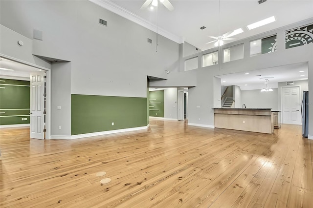 unfurnished living room with ceiling fan, a towering ceiling, crown molding, light hardwood / wood-style flooring, and sink