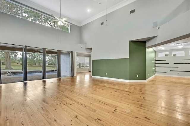 unfurnished living room with ceiling fan, a high ceiling, light hardwood / wood-style flooring, and ornamental molding