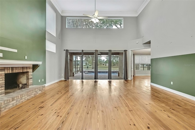 unfurnished living room featuring ceiling fan, a brick fireplace, plenty of natural light, and crown molding