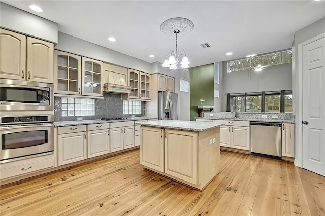 kitchen with appliances with stainless steel finishes, custom exhaust hood, a kitchen island, hanging light fixtures, and a chandelier