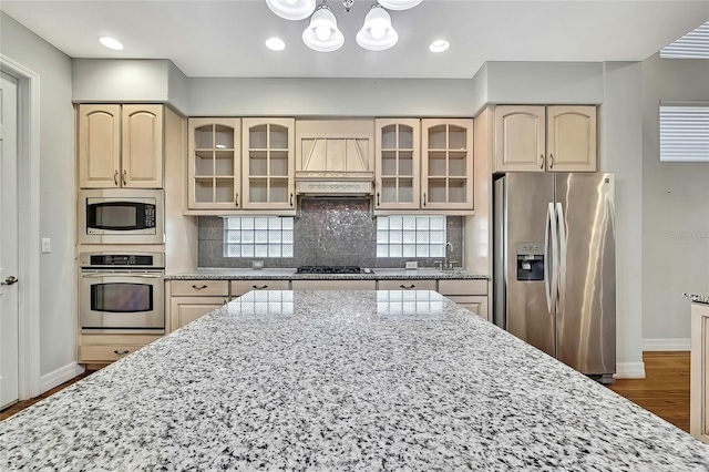 kitchen with light stone countertops, backsplash, appliances with stainless steel finishes, and a notable chandelier