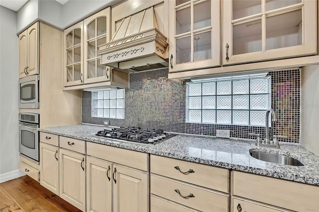 kitchen with premium range hood, light hardwood / wood-style floors, appliances with stainless steel finishes, light stone countertops, and sink