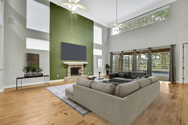 living room featuring ceiling fan, light hardwood / wood-style flooring, a high ceiling, and a brick fireplace