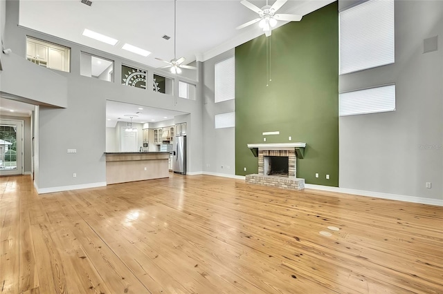 unfurnished living room featuring light hardwood / wood-style floors, ceiling fan, a brick fireplace, and a towering ceiling