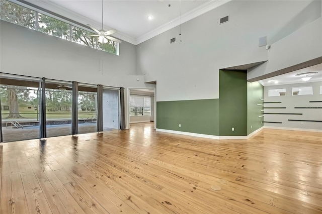 unfurnished living room with ceiling fan, light hardwood / wood-style floors, a high ceiling, and ornamental molding
