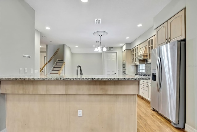 kitchen featuring hanging light fixtures, stainless steel appliances, light stone counters, light hardwood / wood-style floors, and an inviting chandelier