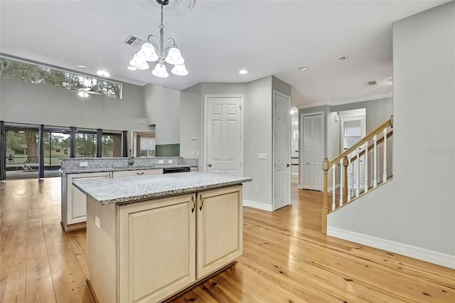 kitchen with light stone countertops, a kitchen island, decorative light fixtures, an inviting chandelier, and light hardwood / wood-style floors