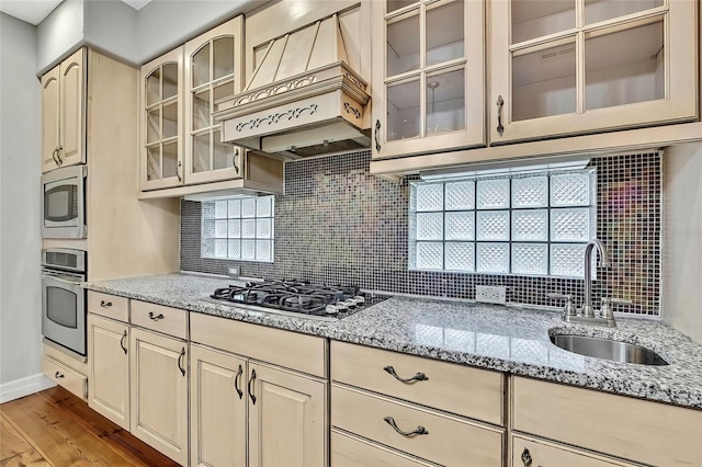 kitchen with custom exhaust hood, sink, light wood-type flooring, stainless steel appliances, and light stone counters
