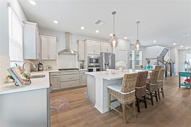 kitchen featuring appliances with stainless steel finishes, wall chimney exhaust hood, a kitchen island, sink, and hanging light fixtures