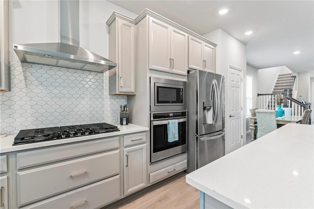 kitchen featuring backsplash, wall chimney range hood, light hardwood / wood-style flooring, and stainless steel appliances