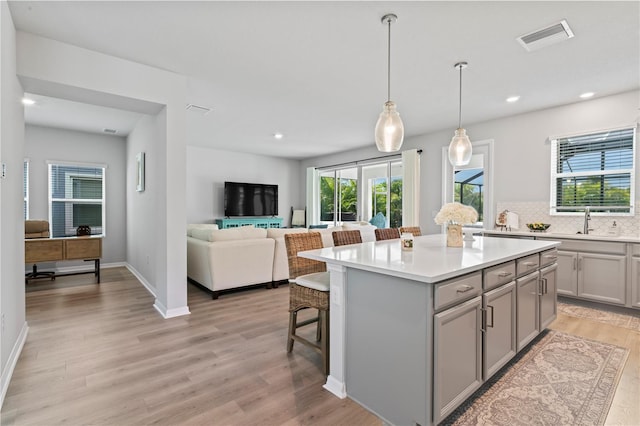 kitchen with a kitchen bar, gray cabinets, backsplash, decorative light fixtures, and a kitchen island