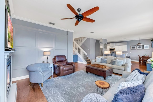 living room featuring ceiling fan, ornamental molding, and dark wood-type flooring