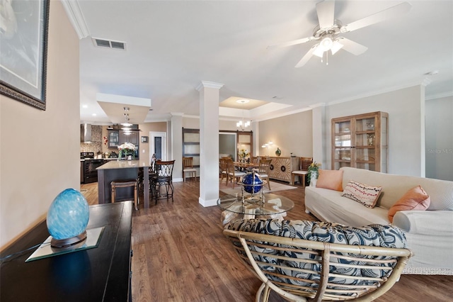 living room with dark hardwood / wood-style flooring, crown molding, ceiling fan with notable chandelier, and decorative columns