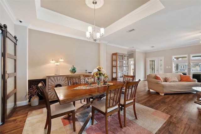 dining room with wood-type flooring, a chandelier, a tray ceiling, crown molding, and a barn door