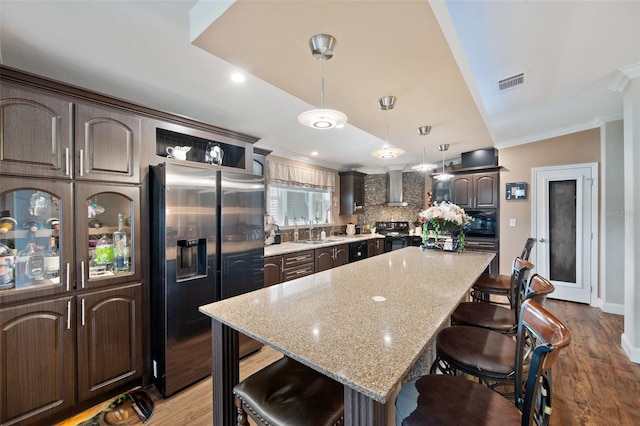 kitchen featuring a breakfast bar, a center island, dark brown cabinetry, and black appliances