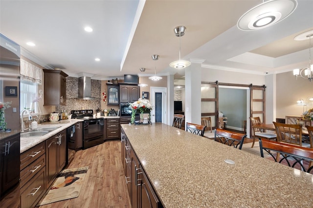 kitchen with black appliances, wall chimney range hood, sink, dark brown cabinets, and a barn door