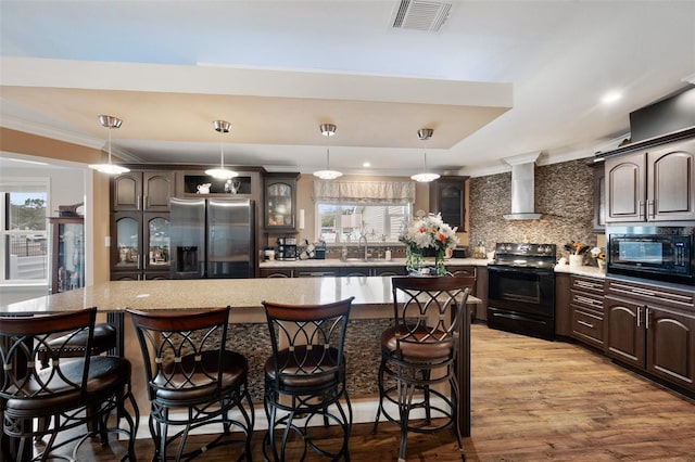 kitchen with a kitchen island, wall chimney range hood, dark brown cabinets, and black appliances