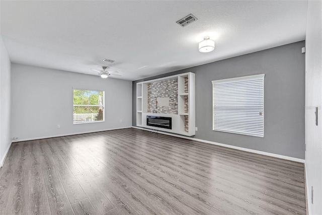 unfurnished living room with ceiling fan, built in shelves, light hardwood / wood-style flooring, and a textured ceiling