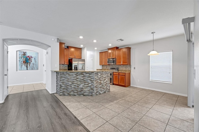 kitchen featuring tasteful backsplash, hanging light fixtures, light tile patterned floors, kitchen peninsula, and stainless steel appliances