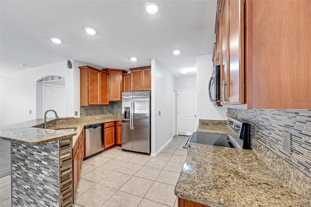 kitchen featuring kitchen peninsula, appliances with stainless steel finishes, sink, light tile patterned floors, and light stone countertops