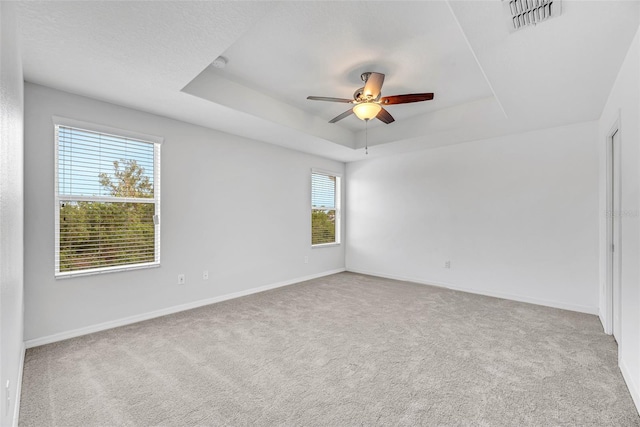 carpeted empty room featuring ceiling fan and a raised ceiling