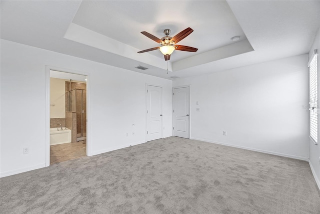 unfurnished bedroom featuring connected bathroom, ceiling fan, a raised ceiling, and light colored carpet