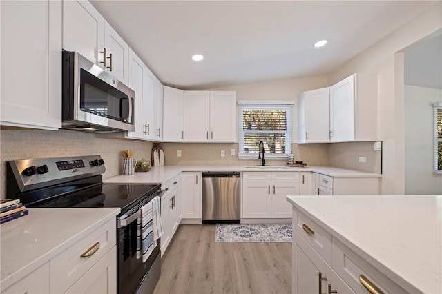 kitchen with light wood-style flooring, a sink, white cabinets, appliances with stainless steel finishes, and backsplash