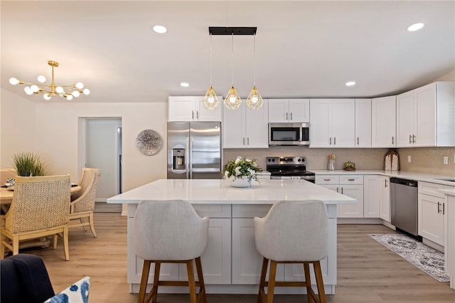 kitchen with appliances with stainless steel finishes, light countertops, hanging light fixtures, and white cabinetry