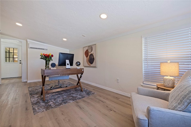 office space featuring baseboards, a textured ceiling, light wood finished floors, and a wall mounted AC