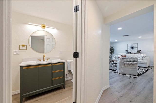 bathroom with visible vents, vanity, baseboards, and wood finished floors