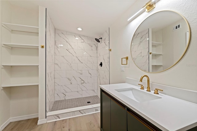 bathroom with wood finished floors, vanity, visible vents, baseboards, and tiled shower