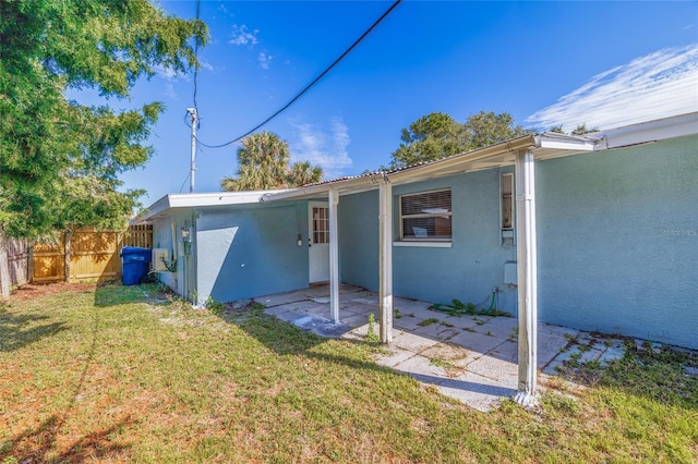 rear view of house with a yard, a patio, fence, and stucco siding