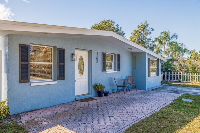 view of front of house with a patio, fence, and stucco siding