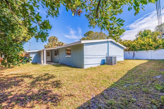 back of property with central AC unit, fence, a lawn, and stucco siding