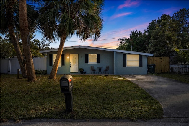 ranch-style house featuring stucco siding, a front yard, driveway, and fence