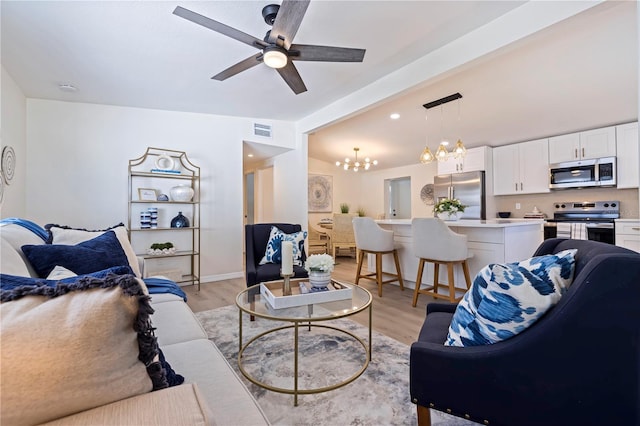 living room featuring visible vents, light wood finished floors, lofted ceiling, and ceiling fan with notable chandelier