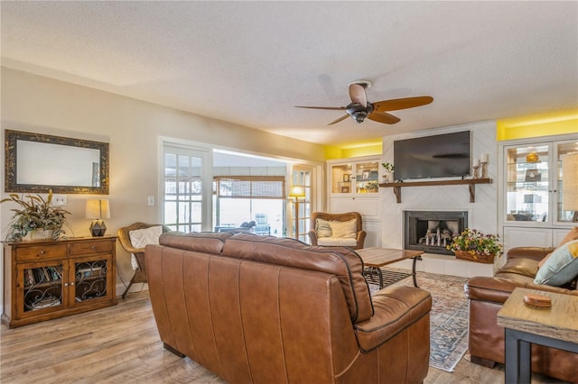 living room with a textured ceiling, ceiling fan, a fireplace, and light hardwood / wood-style flooring