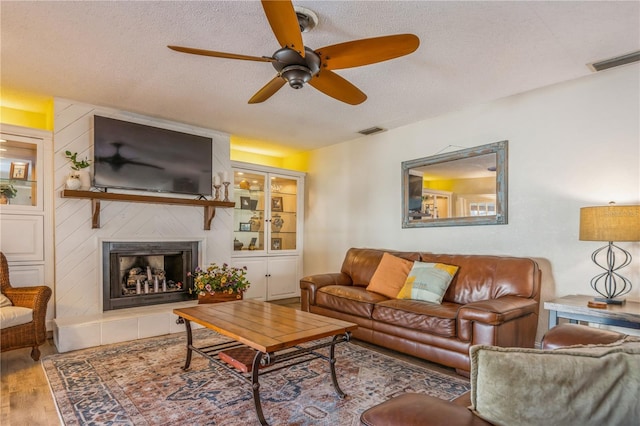 living room featuring ceiling fan, a textured ceiling, wood-type flooring, and a fireplace