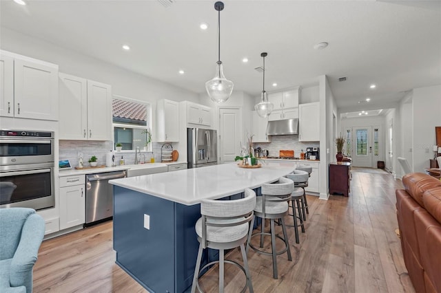 kitchen with pendant lighting, stainless steel appliances, a center island, and white cabinets