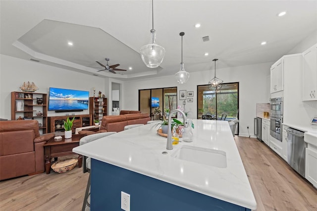 kitchen with hanging light fixtures, a tray ceiling, stainless steel appliances, light stone countertops, and a kitchen island with sink