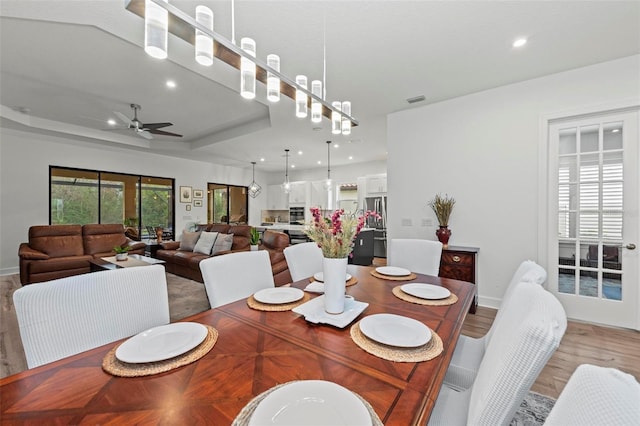 dining area with ceiling fan, a tray ceiling, and light hardwood / wood-style flooring