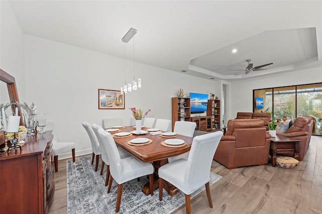 dining room with a tray ceiling, ceiling fan with notable chandelier, and light hardwood / wood-style flooring