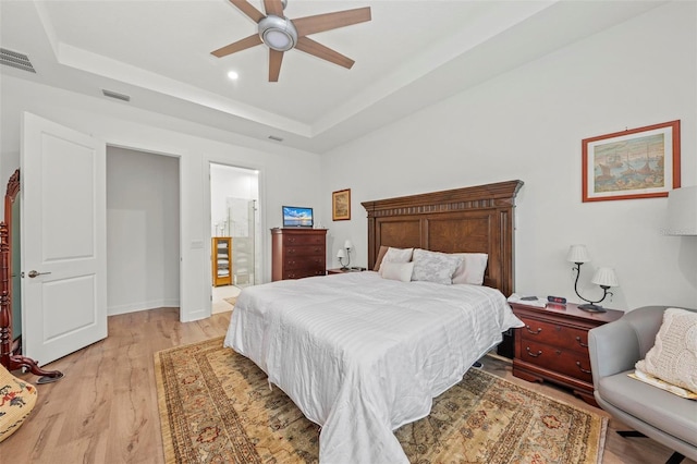 bedroom with a raised ceiling, ensuite bathroom, ceiling fan, and light hardwood / wood-style floors