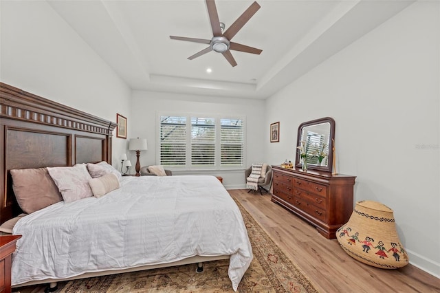 bedroom featuring ceiling fan, a raised ceiling, and light hardwood / wood-style flooring