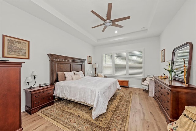 bedroom featuring a raised ceiling, ceiling fan, and light wood-type flooring